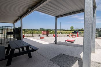 A picnic area with a black table and picnic benches under a metal roof.